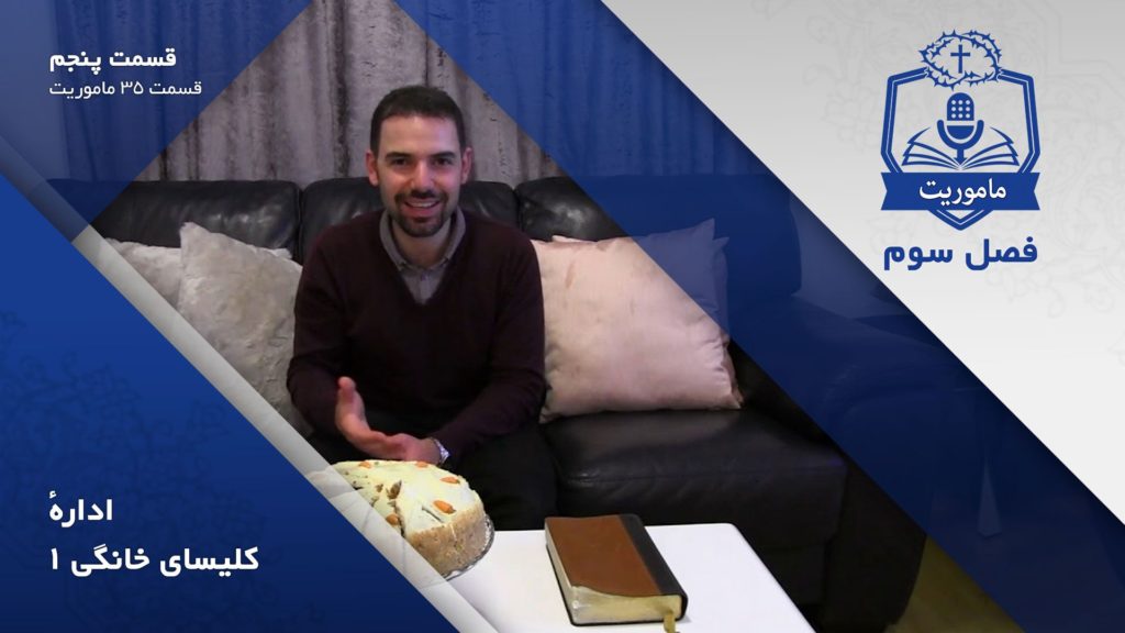 Man smiling while sitting on a couch with a cake and a book on the table.