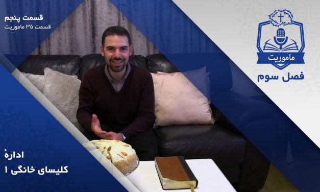 Man smiling while sitting on a couch with a cake and a book on the table.