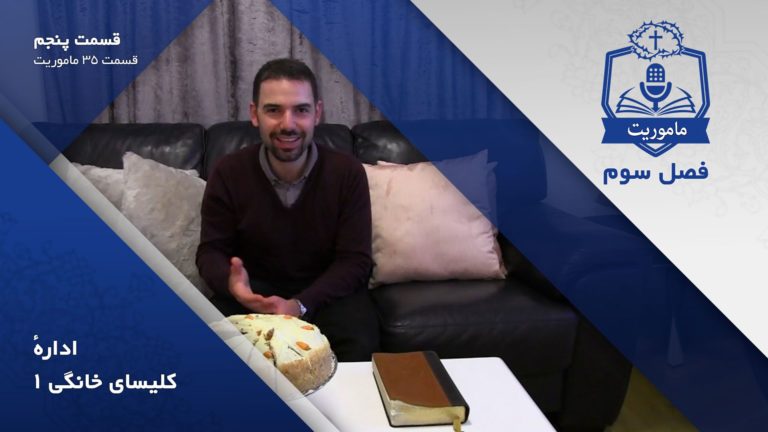 Man smiling while sitting on a couch with a cake and a book on the table.