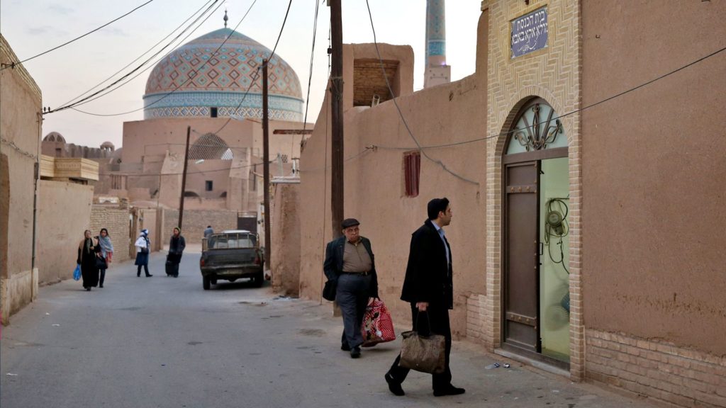 People walking near a mosque with traditional architecture in a narrow street.
