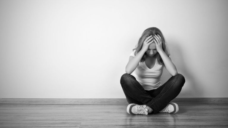 Person sitting on floor, covering face, in a minimalistic room.