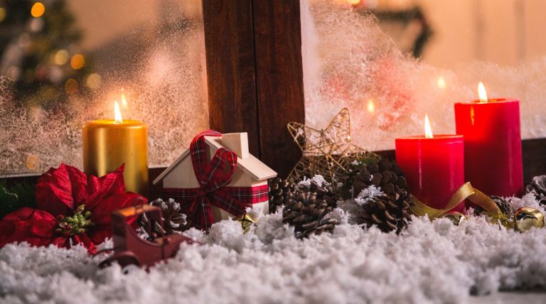 Festive Christmas decorations with candles, presents, pinecones, and artificial snow by a foggy window.