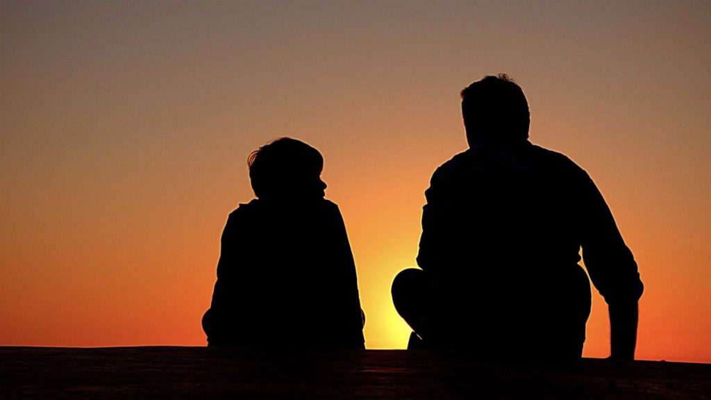 Silhouettes of two people sitting against a vibrant sunset sky.