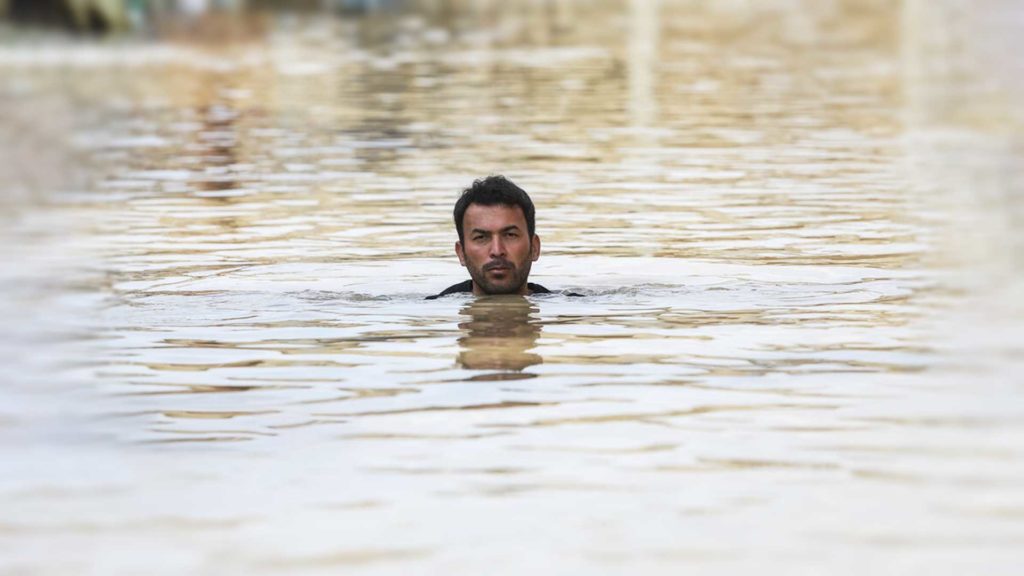 Man swimming in calm, shallow water with head above surface.