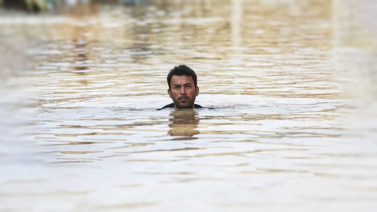Man swimming in calm, shallow water with head above surface.