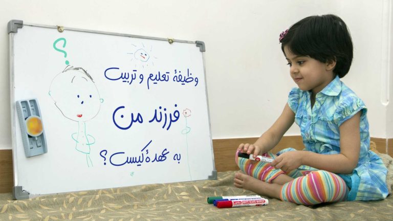 A child playing with toys beside a whiteboard with Persian writing.