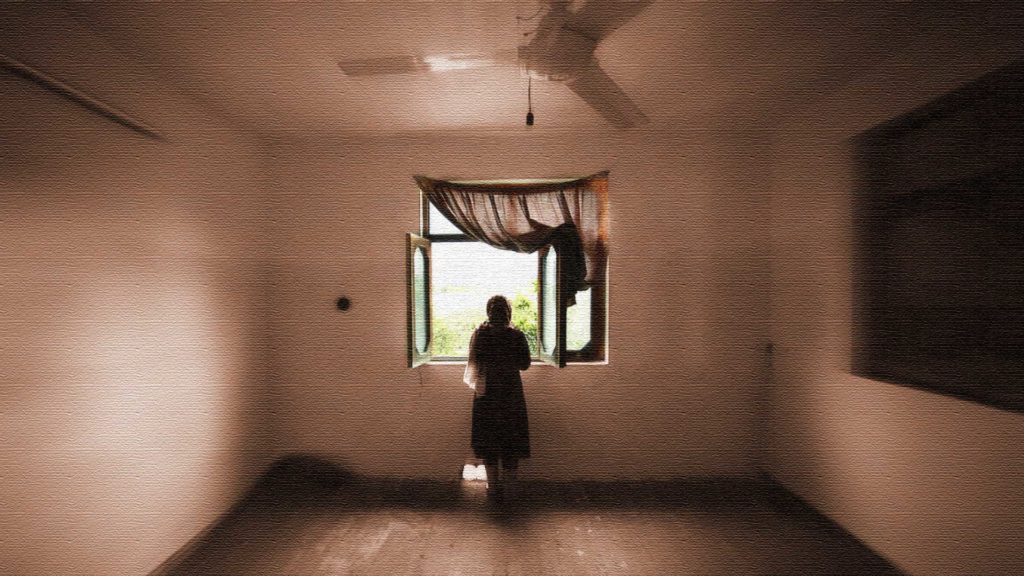 A lone person stands by a window in an empty room.