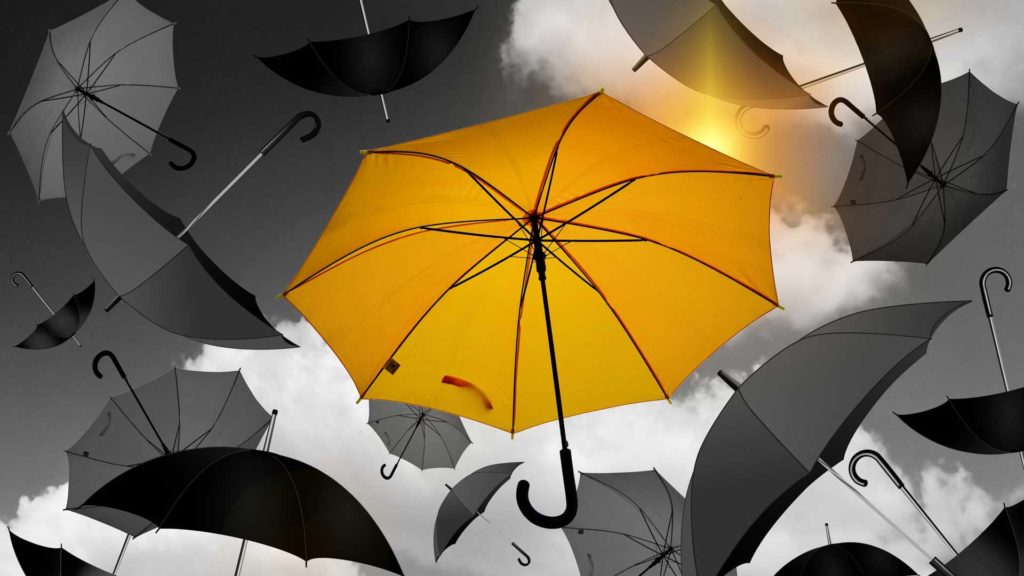 A vibrant yellow umbrella stands out among black umbrellas.