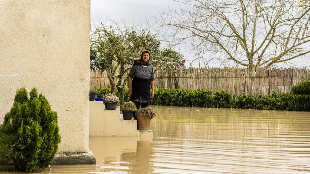 Person standing on a ledge near floodwaters with trees in the background.