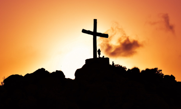 Silhouette of a cross on a hill during sunset.