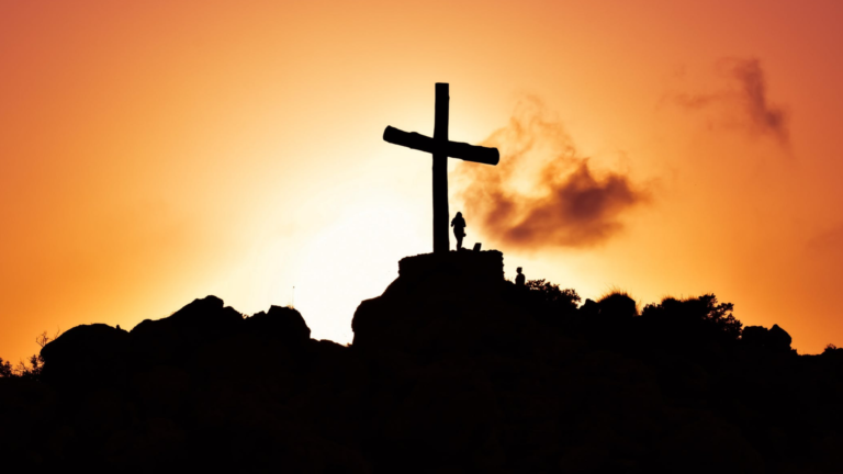 Silhouette of a cross on a hill during sunset.