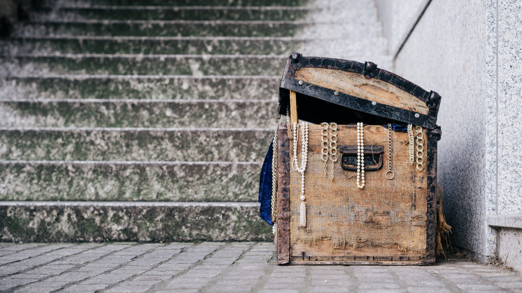 Old wooden box with jewelry and a mirror on stone stairs.