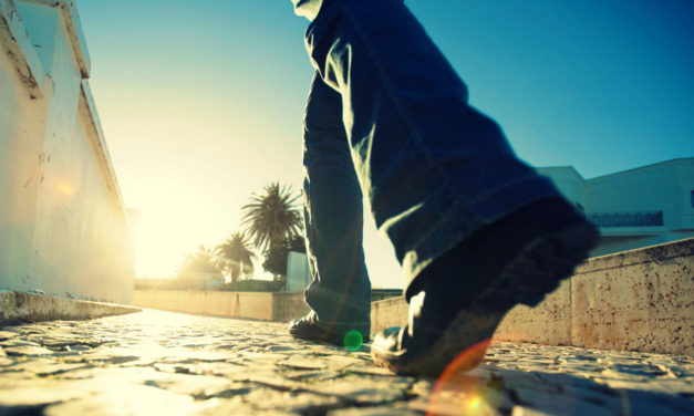 Close-up of a person walking on a sunlit street with palm trees in the background.