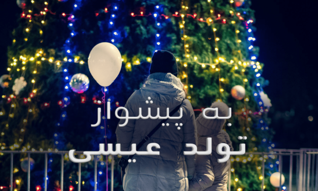 A person holding a child in front of colorful Christmas lights.